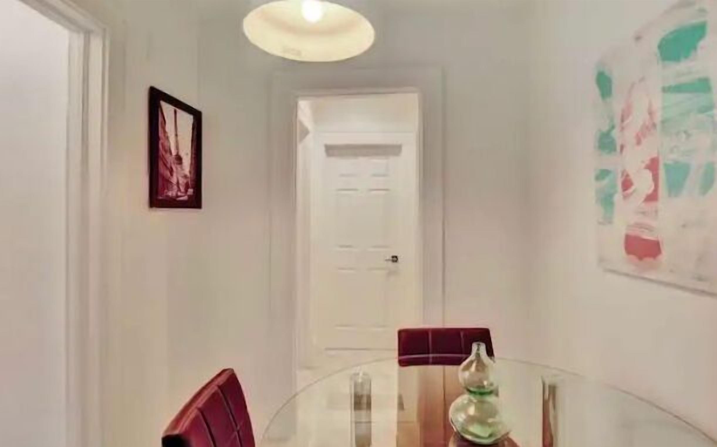 Un coin repas avec une table en verre, des chaises rouges et une porte blanche en arrière-plan.