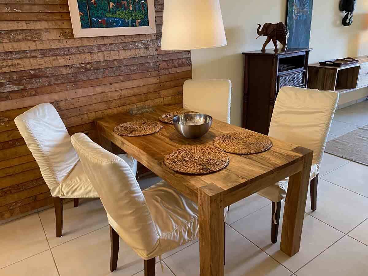 Une table de salle à manger en bois, accompagnée de quatre chaises, d’un saladier en métal et de sets de table en fibres tressées.