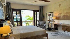 A bedroom with a large bed, a desk, a chair, and a view of the ocean.