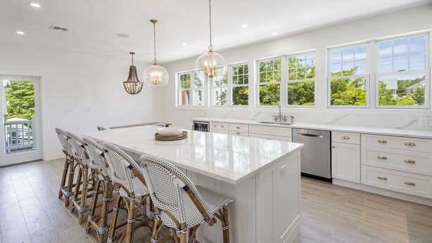 Een moderne keuken met witte kastjes, een groot kookeiland met barkrukken en hanglampen.