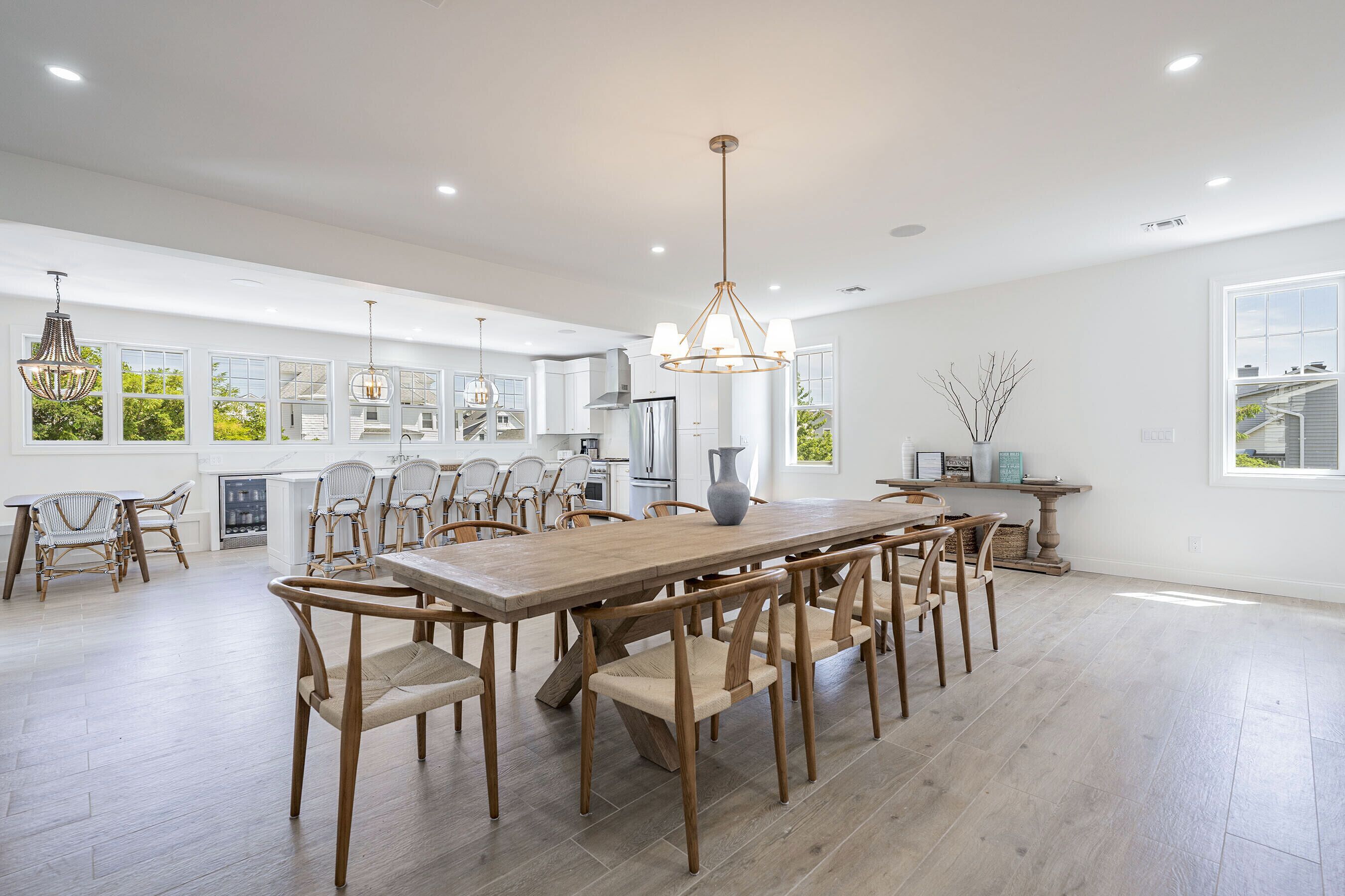 A spacious kitchen with a large wooden table and chairs, modern appliances, and large windows offering views of greenery.