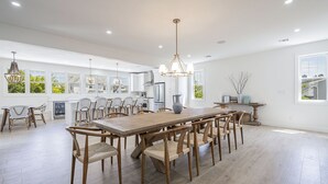 Een ruime keuken met een grote houten tafel en stoelen, moderne apparatuur en ramen met uitzicht op groen.