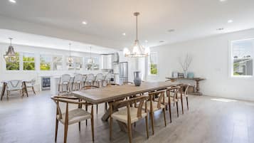 A spacious kitchen with a large wooden table and chairs, modern appliances, and large windows offering views of greenery.