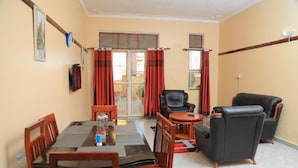 A dining area with a table set for four, a black leather sofa, and a chair. - City Oasis - 2 Bedroom Apartment in Kampala (Kampala)
