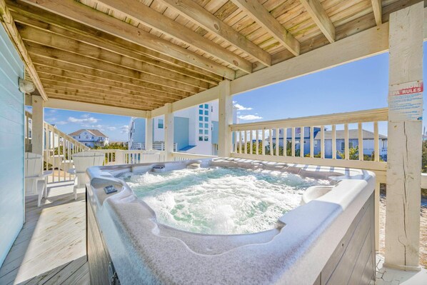 Un bain à remous situé sous une terrasse en bois, avec vue sur les maisons au loin.