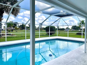 Ein überdachter Pool mit Blick auf eine Rasenfläche und Palmen.