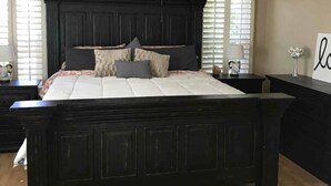 A bedroom with a dark wooden bed frame, a white bedspread, and multiple pillows. There are two bedside tables with lamps and a small vase with flowers. - 🔥HEATED Pool, Pool Table, Golf, and Spring Training (Glendale)
