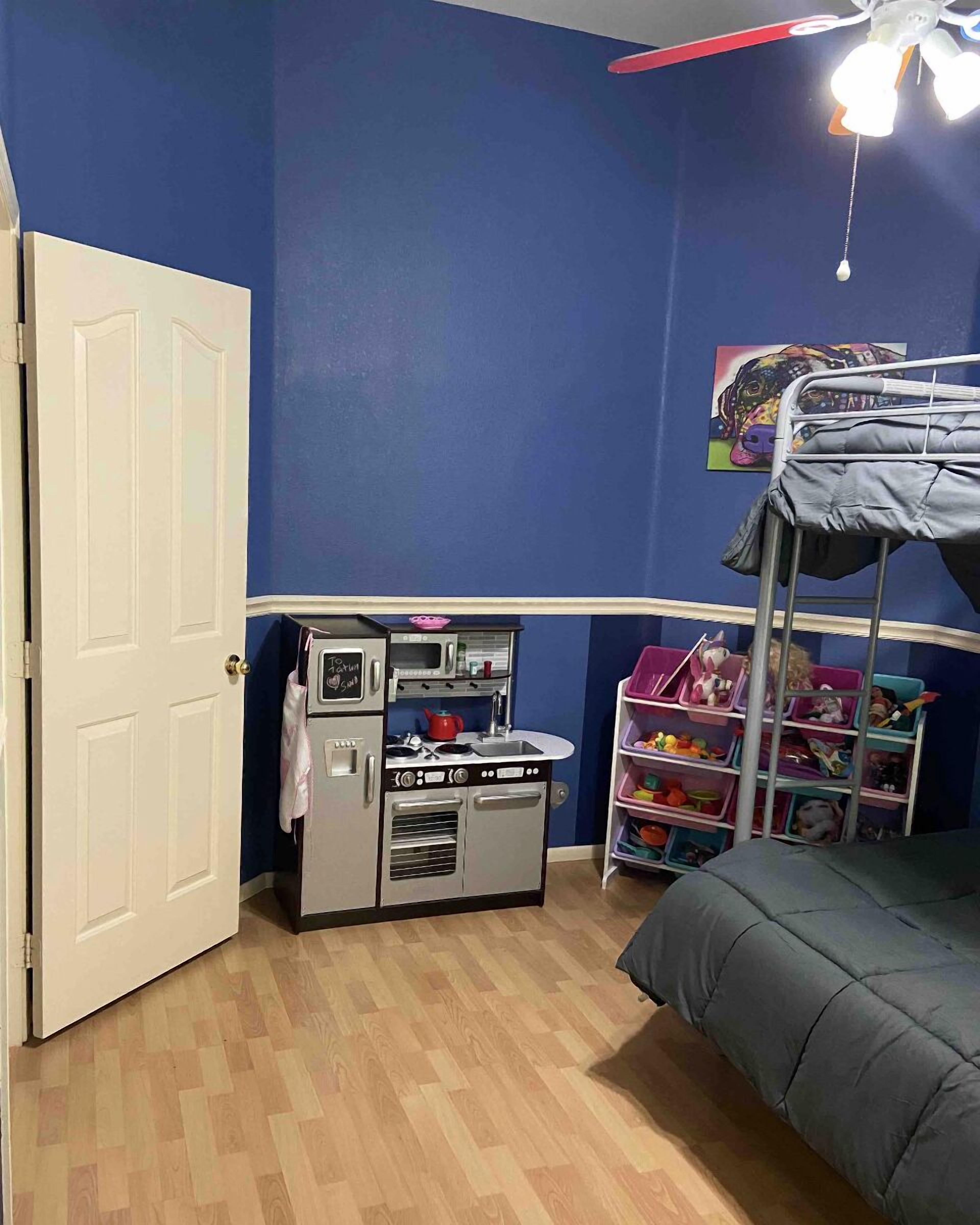 A room with a bunk bed, a kitchenette with a microwave and stove, and a toy shelf.