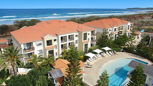 A beachfront hotel with multiple balconies, a swimming pool, and a view of the ocean.