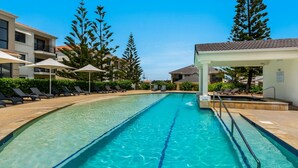 A swimming pool with lounge chairs and umbrellas, surrounded by buildings and trees.
