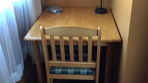 A small wooden table with a chair, a lamp, and a remote control.