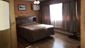 A bedroom with a bed, a ceiling fan, a bedside table with a lamp, a framed picture on the wall, and a window with curtains.