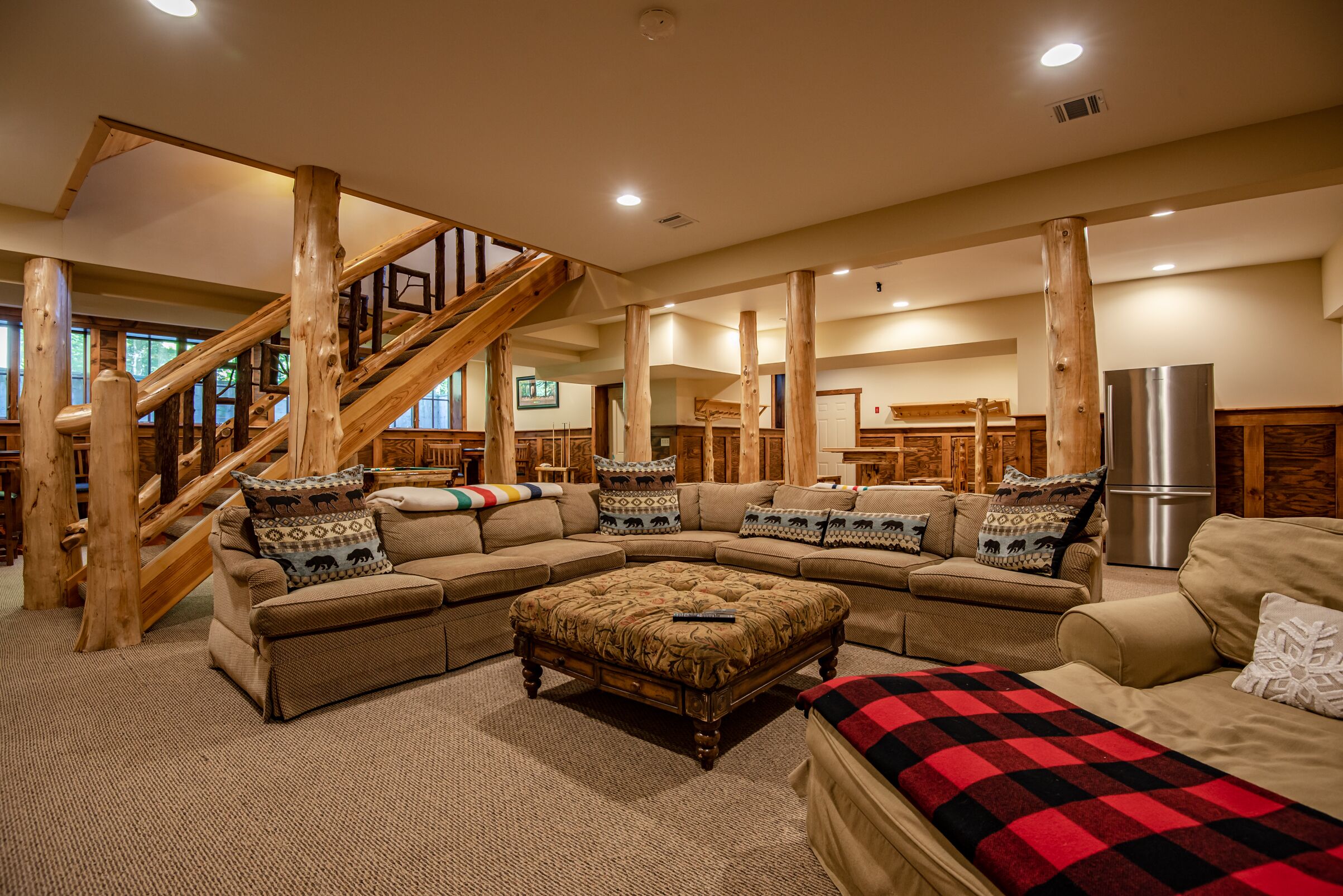 A spacious living room with a large sectional sofa, a wooden staircase, and a kitchen area in the background.