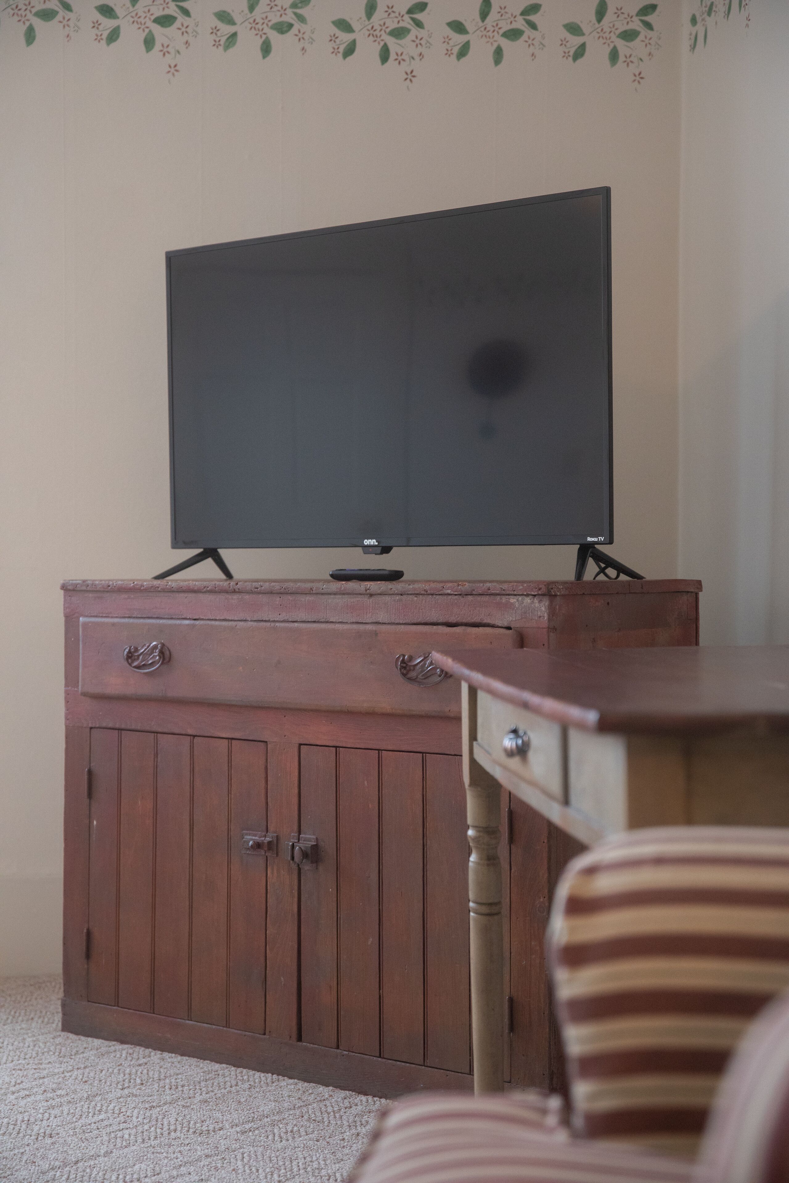 A wooden cabinet with a flat-screen TV on top, a striped chair, and a carpeted floor.