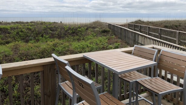 Une terrasse en bois avec des bancs, donnant sur une plage et des dunes.