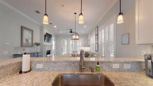 A kitchen with granite countertops, stainless steel sink, pendant lights, and a ceiling fan. - Poolside Cottage 57 - Magnolia Cottage The Cottages at Jekyll Island Poolside (Jekyll Island)