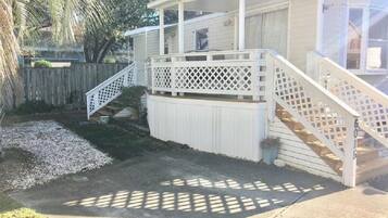 A covered outdoor area with a wooden deck, a white fence, and a staircase leading to a covered porch.