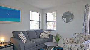Una sala de estar con un sofá gris, un sillón estampado, una mesita redonda y un cuadro de un velero en la pared.
