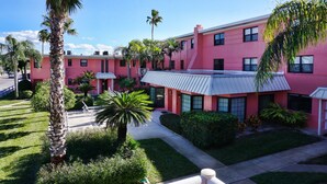 Un edificio rosa con un corredor cubierto y palmeras.