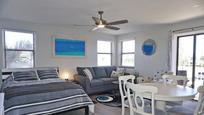 Un dormitorio con cama, sofá gris, mesa de comedor con sillas y ventilador de techo.