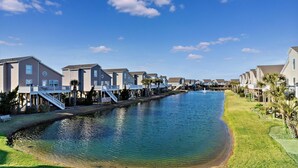 Un quartier résidentiel bordé de maisons le long d’un canal, avec un ciel dégagé et une eau calme.