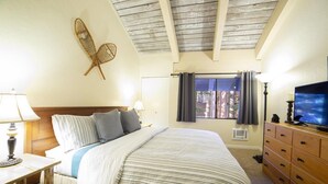 A hotel room with a bed, wooden headboard, a television, a dresser, a window with curtains, and a wall-mounted decorative item.