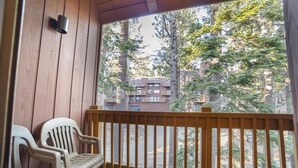 A wooden balcony with a view of tall trees and a building in the background.