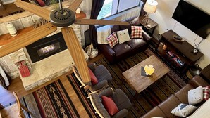 A spacious living room with a fireplace, leather sofa, wooden coffee table, and a ceiling fan.