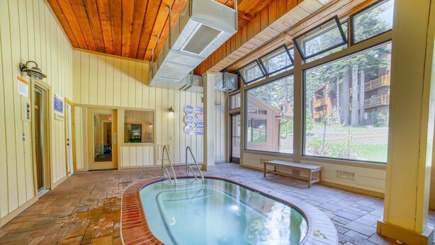 A swimming pool with a wooden deck, a bench, and large windows offering a view of the outdoors.