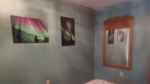 A bedroom with a bed, two wall-mounted pictures of the Northern Lights, and a mirror.