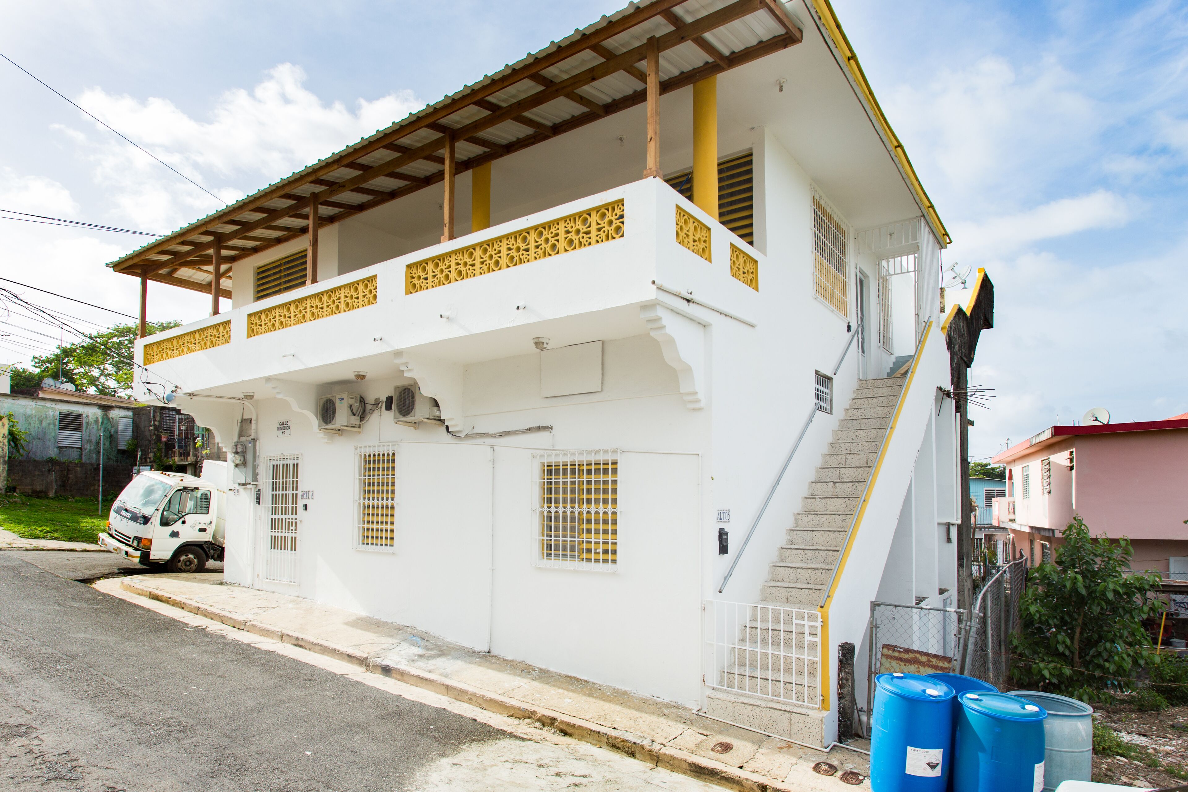 Un edificio blanco con un balcón, una escalera y una furgoneta blanca estacionada.