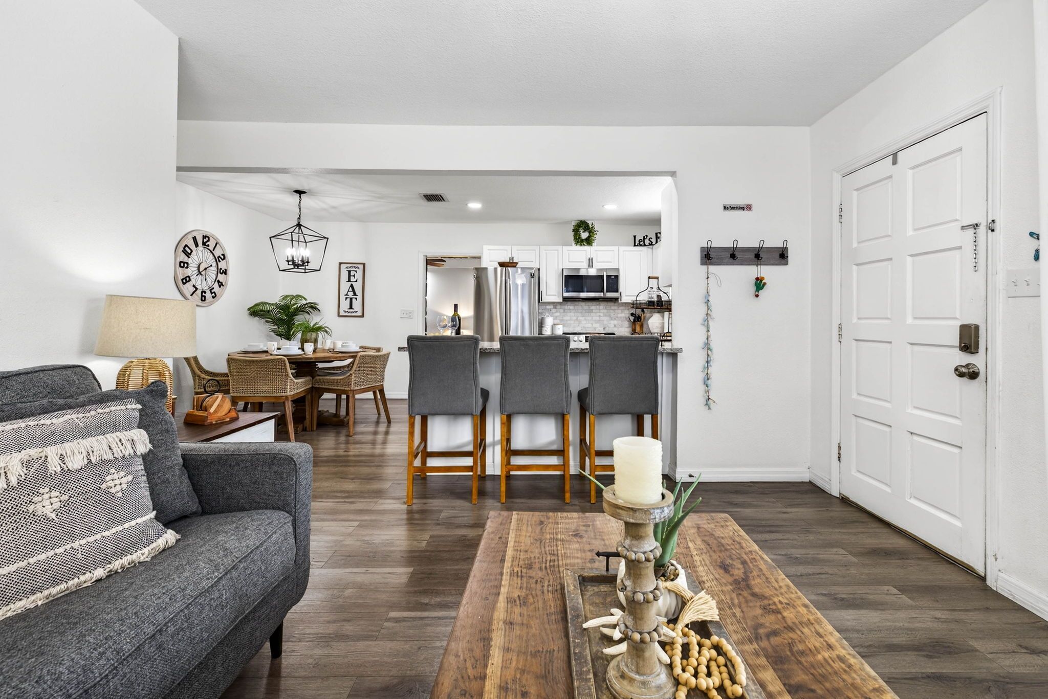 En moderne stue med en grå sofa, et træ sofabord og et spiseområde med grå stole og en lysekrone.
