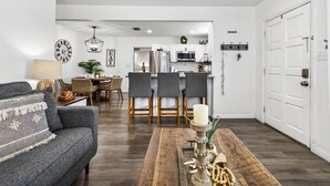 En moderne stue med en grå sofa, et træ sofabord og et spiseområde med grå stole og en lysekrone.