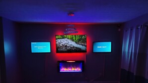 Sistema de cine en casa con un televisor grande, dos pantallas más pequeñas y una chimenea.