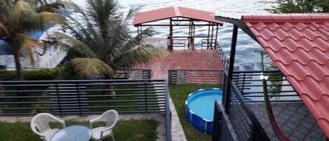 A patio area with a pool, a covered seating area, and a view of the sea.