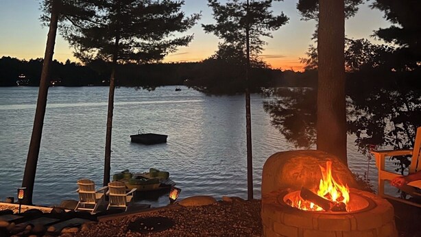 A lakeside outdoor seating area with a fire pit, wooden chairs, and a dock with boats.