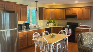 A kitchen with wooden cabinets, a stainless steel refrigerator, a dining table with chairs, and a patterned armchair.