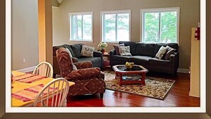 A living room with a sofa, armchair, coffee table, and a dining table with chairs.