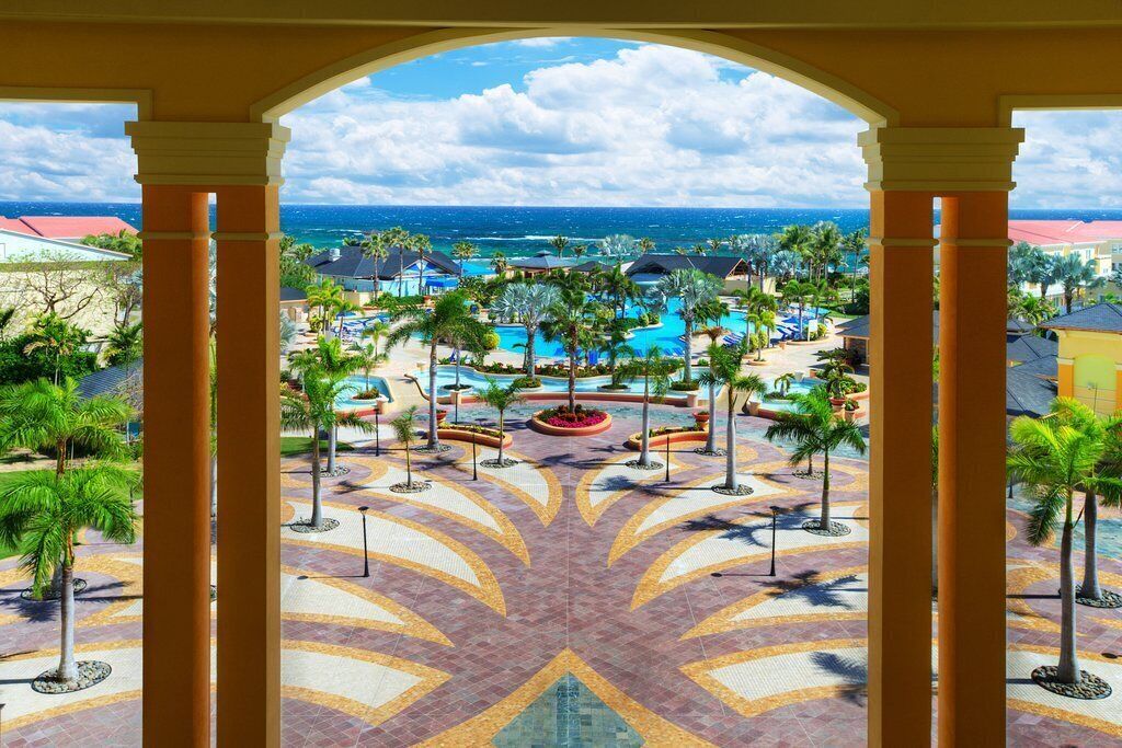 A resort view with a pool, palm trees, and a view of the ocean.