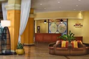 A reception area with a large wall map, a wooden reception desk, a brown sofa with striped cushions, and a potted plant. - St Kitts | Family Shore Stay | Pool + Beach | 2BR Condo (St. Kitts)