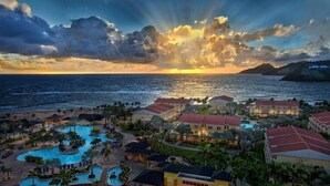 Un resort con varias piscinas, un edificio central y vista al océano al atardecer.