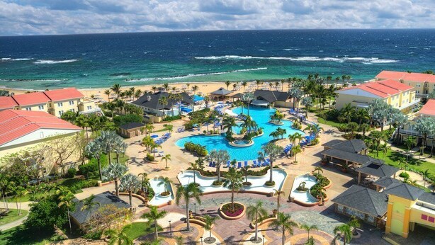 Un resort con piscina central, acceso a la playa y vistas al océano.