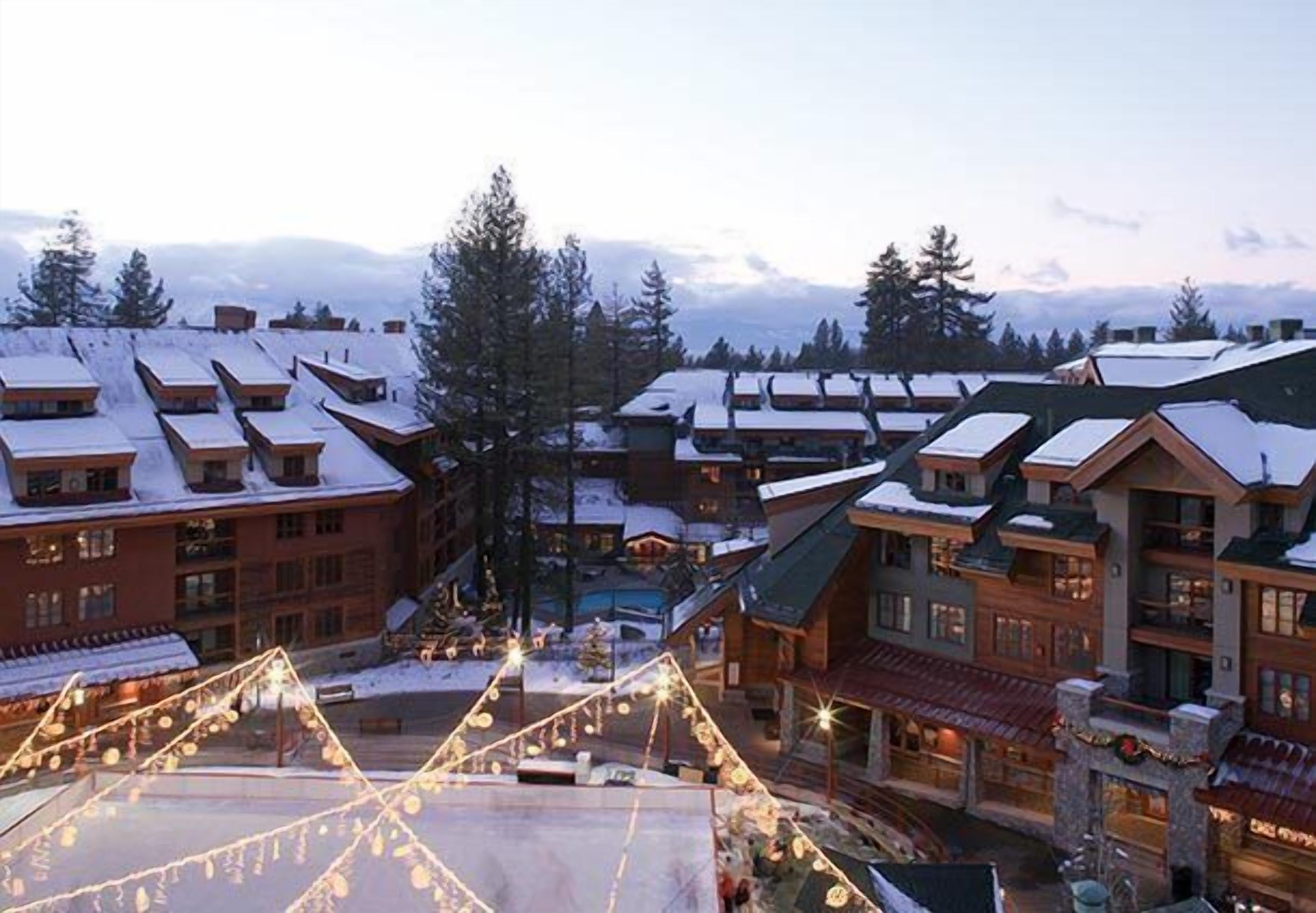 A resort with multiple buildings, some with snow-covered roofs, and a central area with lights.
