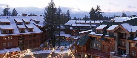 A resort with multiple buildings, some with snow-covered roofs, and a central area with lights.