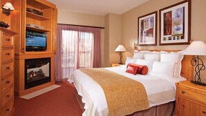 A hotel room with a bed, a television, a fireplace, a window with curtains, and artwork on the wall.