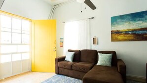 Una habitación con un sofá marrón, un tapete azul estampado, una puerta amarilla y un cuadro en la pared.