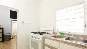 Una cocina con armarios blancos, estufa a gas, un lavaplatos y una ventana con persianas.