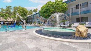 A pool area with a water fountain, lounge chairs, and a building in the background.