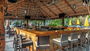 A bar area with a wooden counter, wicker chairs, and a thatched roof.