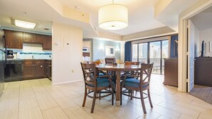 A modern kitchen with dark wooden cabinets, a dining area with a round table and chairs, and a large window providing a view of the city.